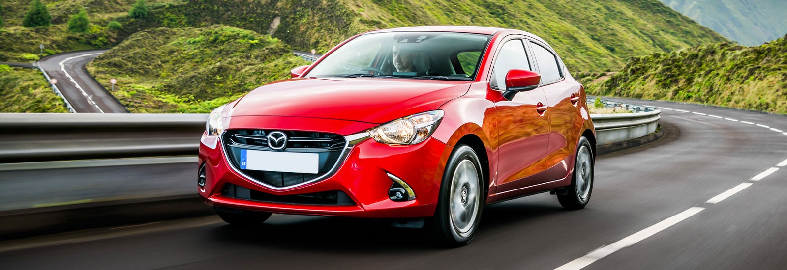 Red Mazda 2 driving, viewed from the front